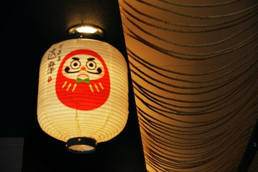 A traditional Japanese lantern with a red circle and a face design, next to a cylindrical structure with horizontal lines.