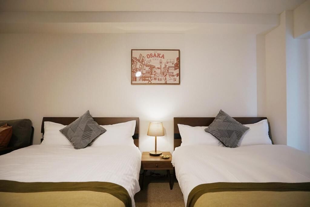 A hotel room with two beds, a nightstand with a lamp, and a framed picture on the wall.