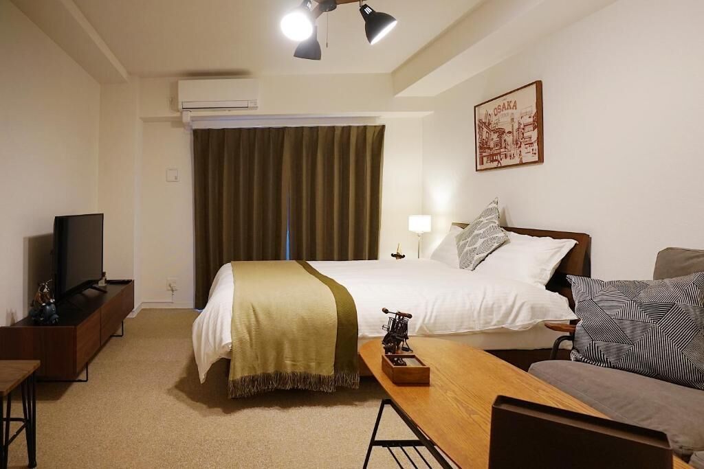 Et hotelværelse med seng, skrivebord, fjernsyn, lampe og et billede på væggen.