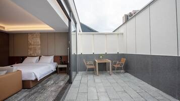 A modern hotel room with a bed, a sofa, a small table with chairs, and a view of the cityscape through large windows.