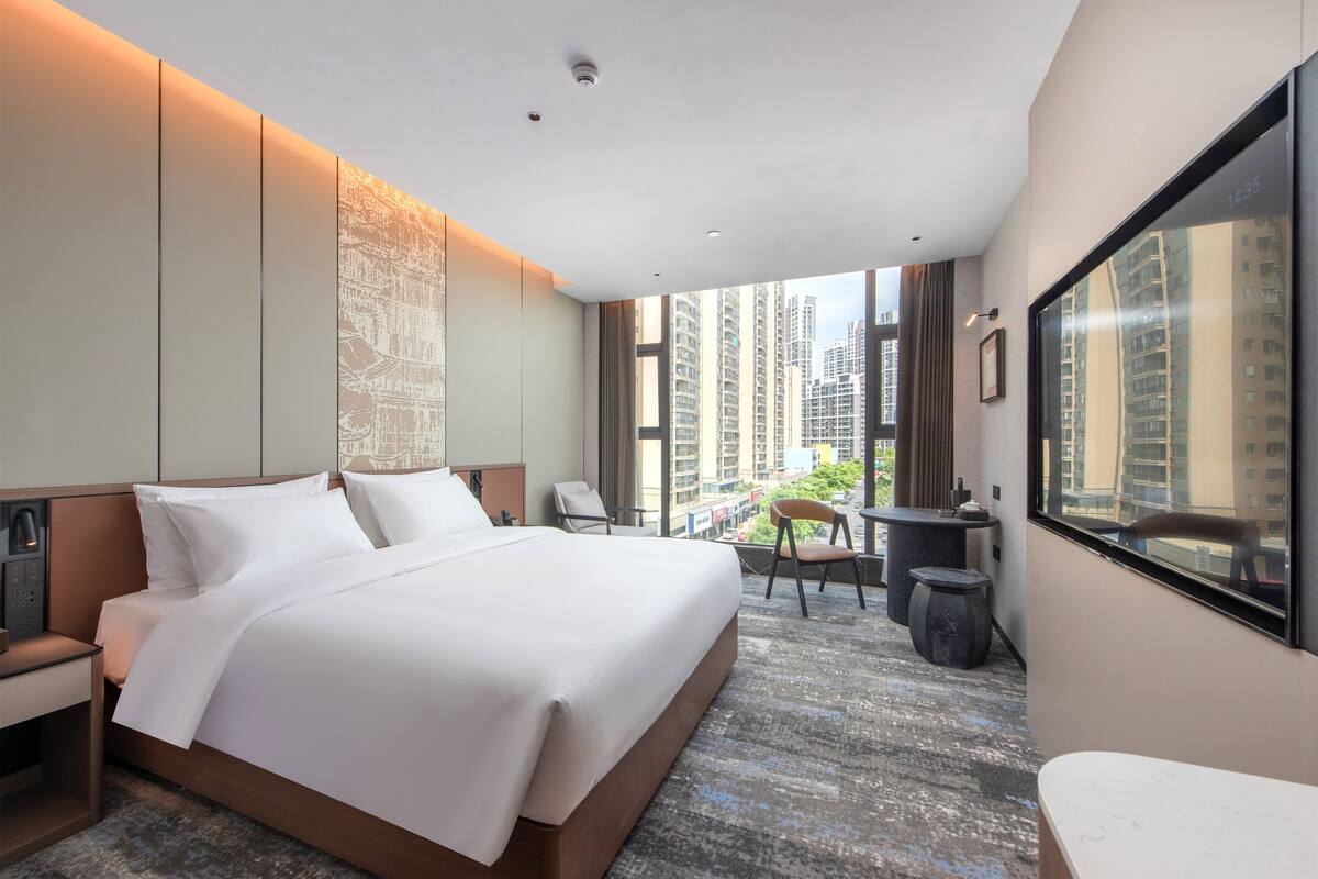 Habitación de hotel moderna con una cama grande, un escritorio y vistas a edificios altos.