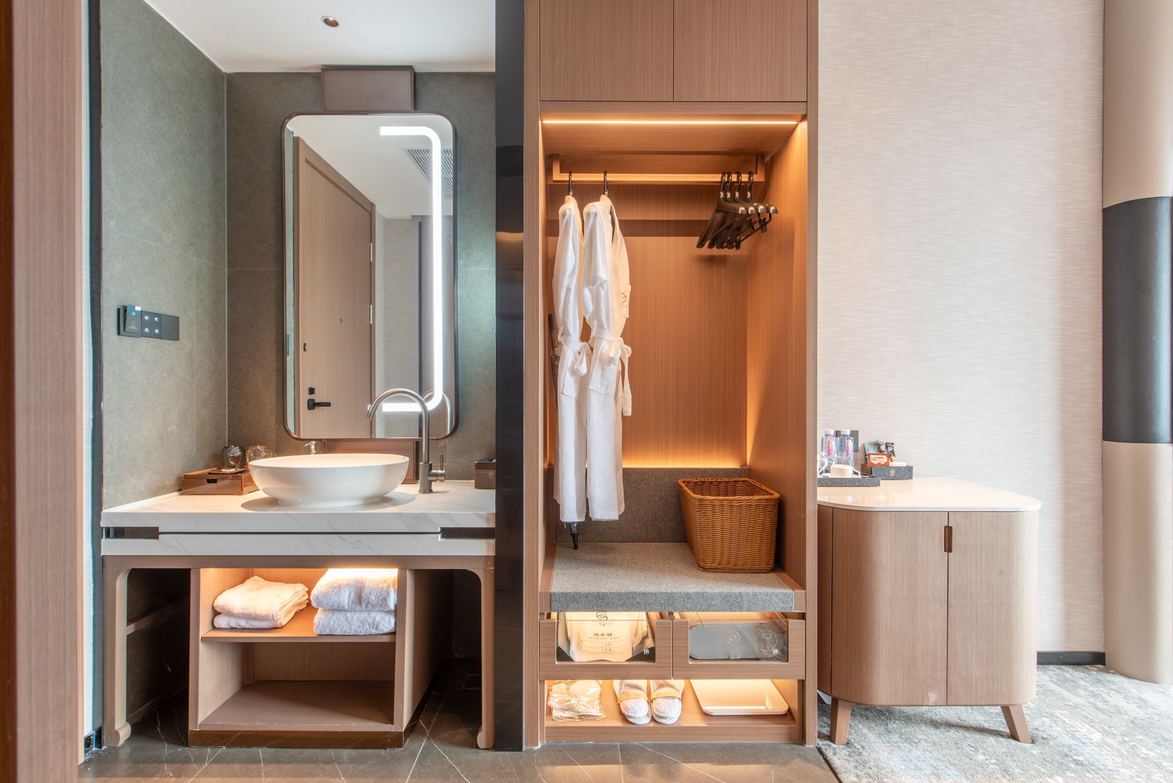 Un baño moderno con un espejo grande, dos lavamanos, un perchero para batas y una cesta.