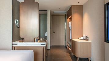 Ein modernes Hotelzimmer mit einem großen Bett, einem Schminktisch mit Spiegel, einem kleinen Schreibtisch und einem begehbaren Kleiderschrank.
