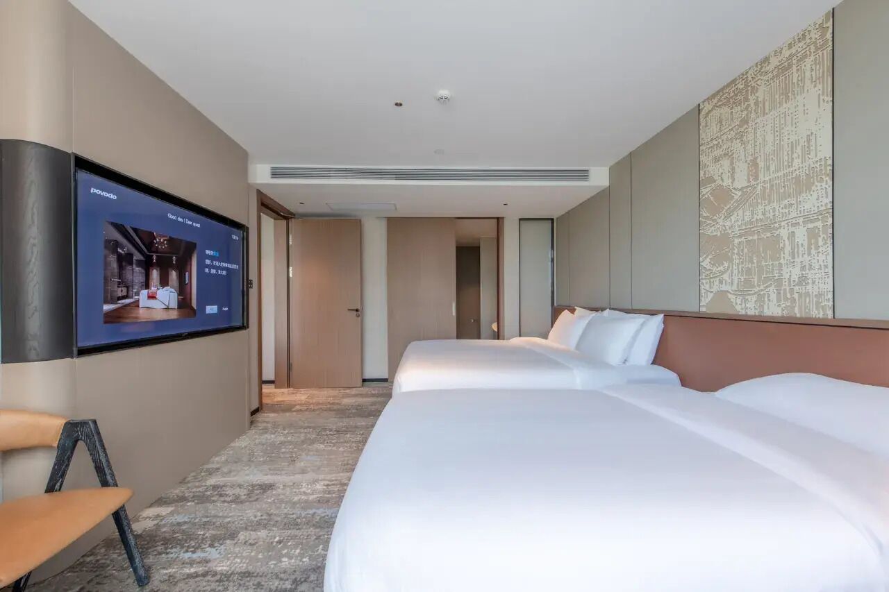 Habitación de hotel con dos camas, un televisor montado en la pared y piso alfombrado.