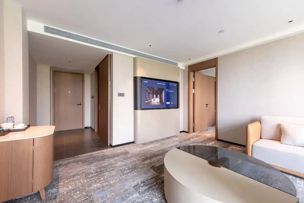 Un moderno vestíbulo de hotel con un mostrador de recepción, un televisor de pantalla plana grande montado en la pared, un sofá y suelo alfombrado.