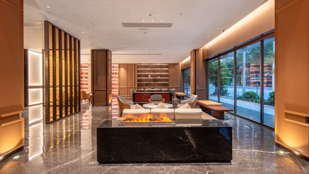 Un vestíbulo moderno con un mostrador de recepción de mármol negro, una zona de estar con sofás y sillones, un elemento decorativo de fuego y grandes ventanales con vistas al exterior.