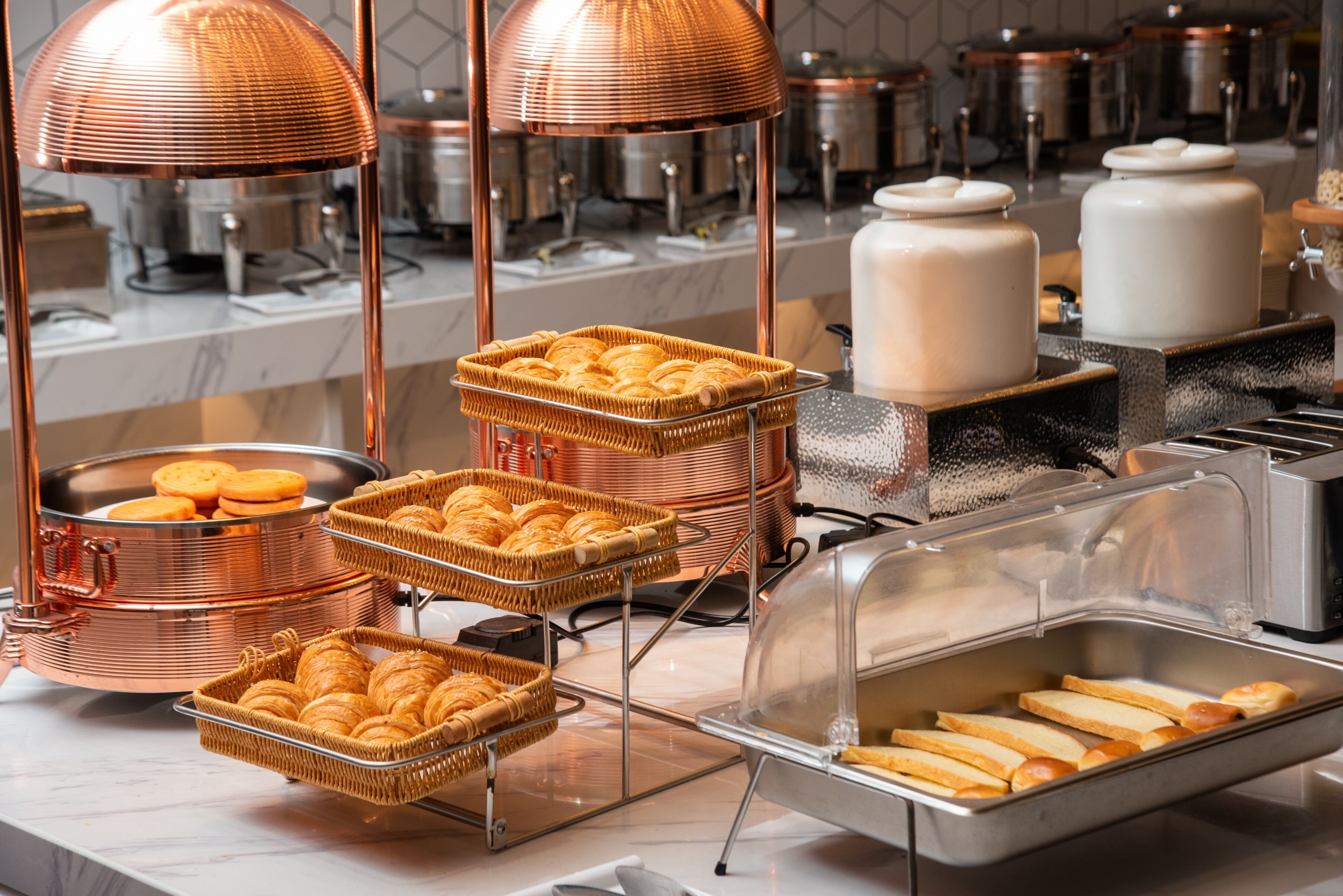Ein reichhaltiges Buffet mit verschiedenen Speisen, darunter Brot und Gebäck, präsentiert auf Kupferständer und Körben.