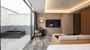 Habitación de hotel moderna con un ventanal grande, televisión de pantalla plana, sofá y una mesita.