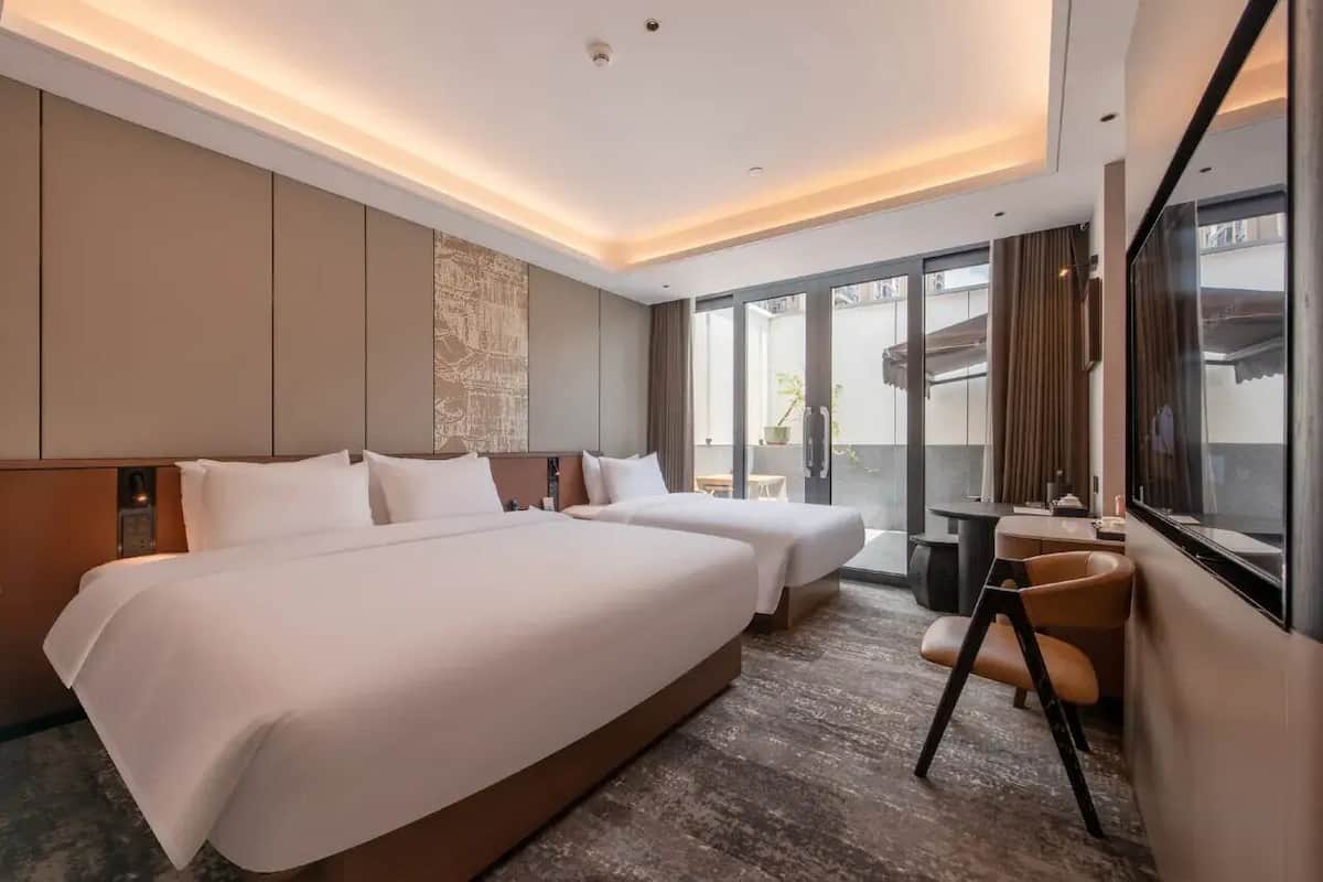 Habitación de hotel con dos camas, un ventanal grande, una mesita y una silla.