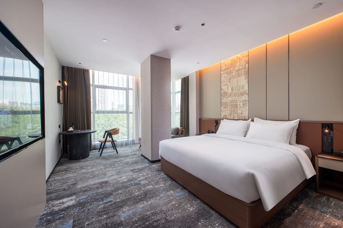 Habitación de hotel moderna con una cama grande, un escritorio y una silla. Hay una ventana con vistas a edificios y una cortina.