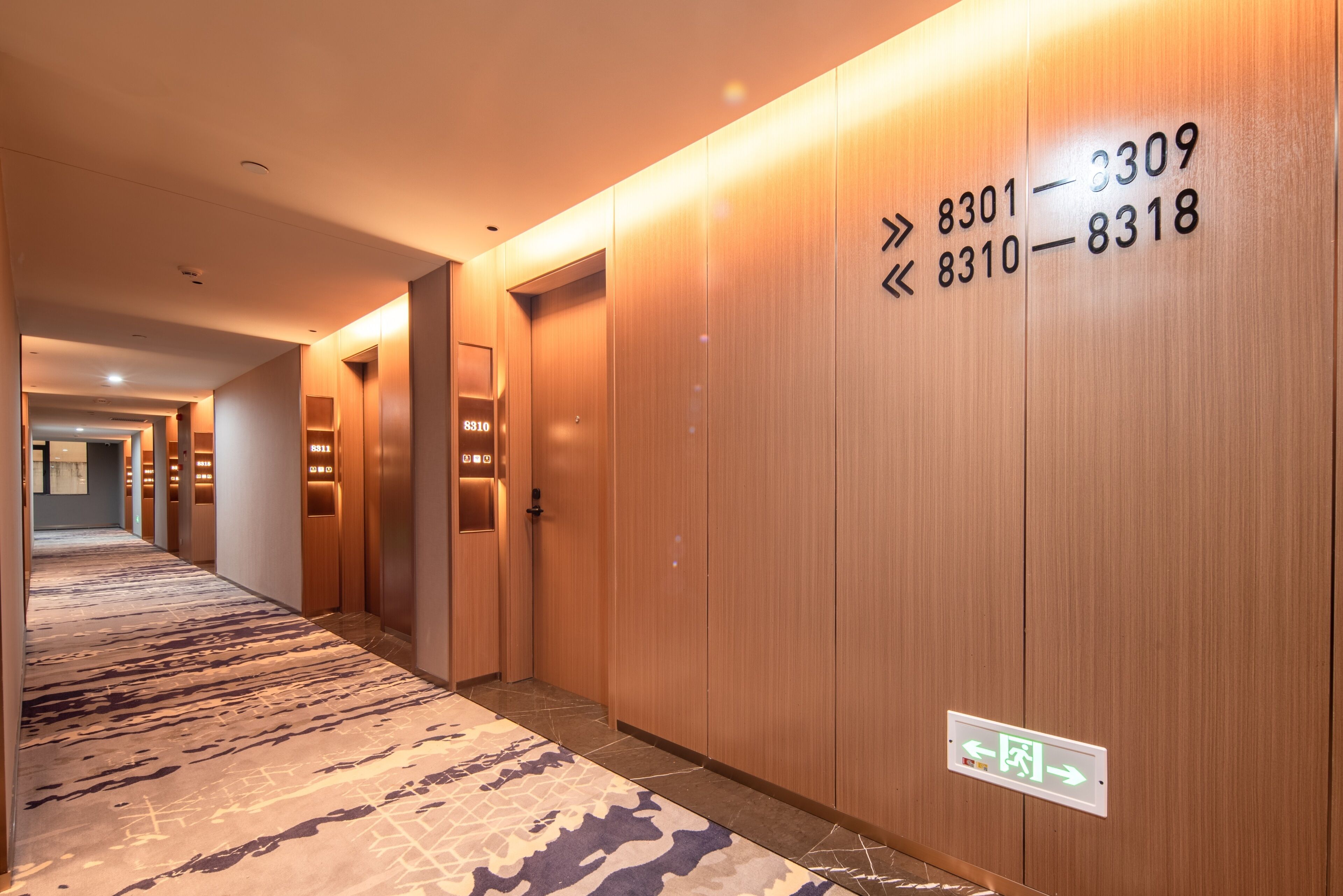 A hotel corridor with wooden walls, numbered doors, and a patterned carpet.