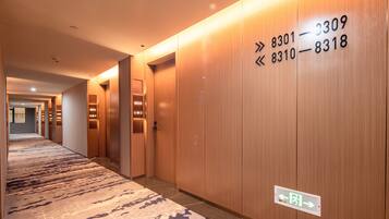A hotel corridor with wooden walls, numbered doors, and a patterned carpet.