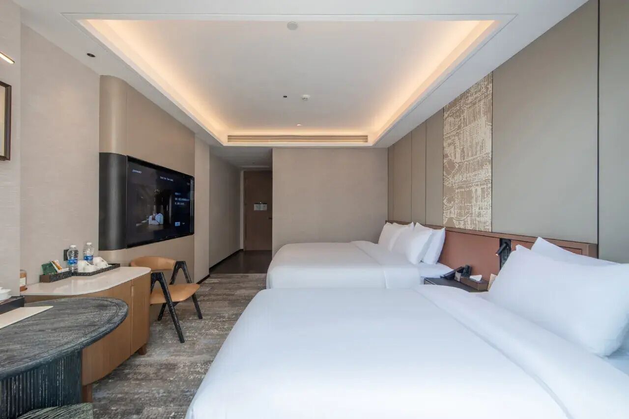 Habitación de hotel con televisión de pantalla plana, dos camas, un escritorio con silla y una obra de arte colgada en la pared.