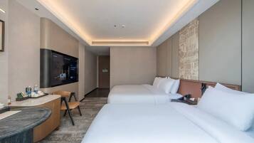 Habitación de hotel con televisión de pantalla plana, dos camas, un escritorio con silla y una obra de arte colgada en la pared.