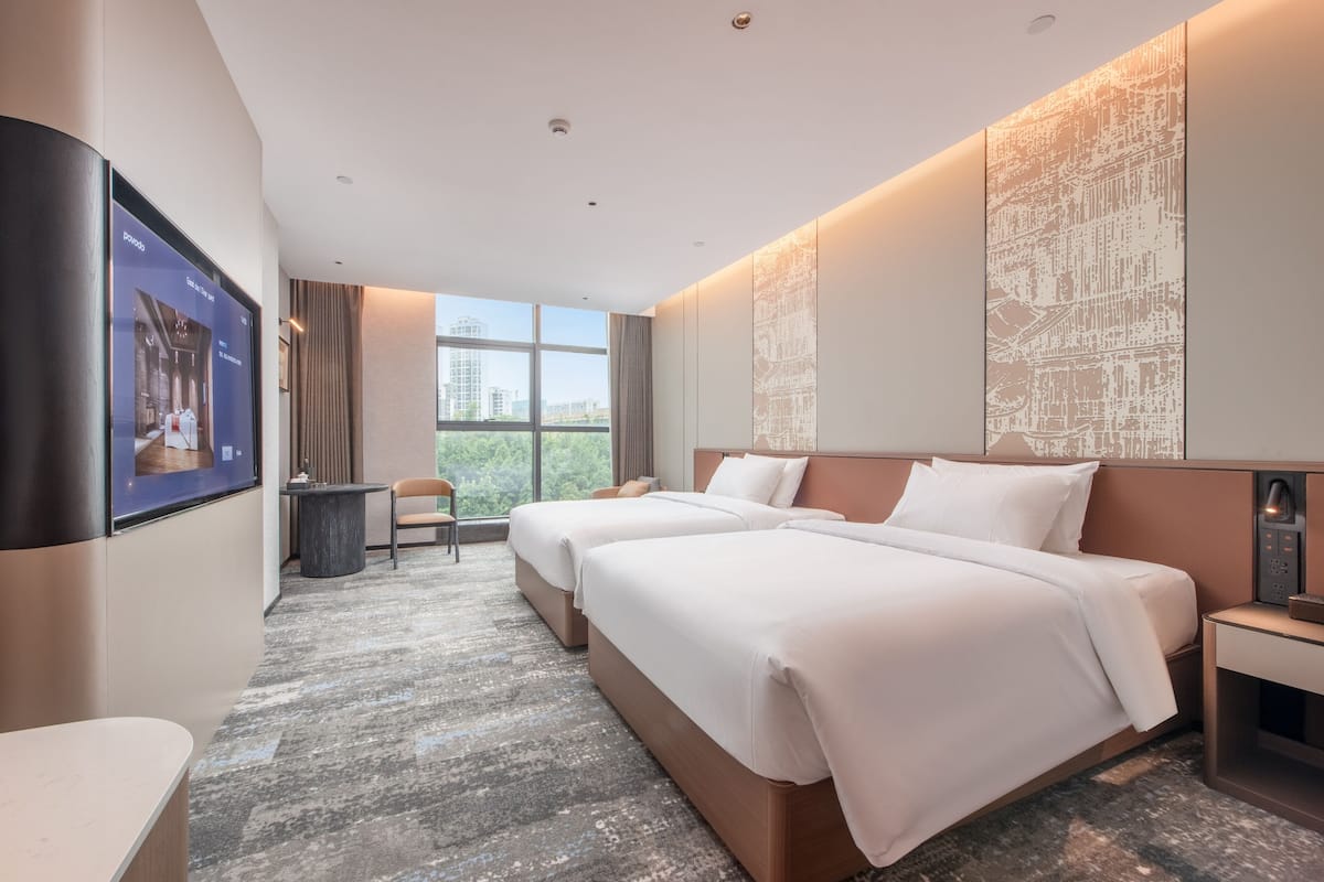 Habitación de hotel con dos camas, un escritorio, una silla y un ventanal con vistas a la ciudad.
