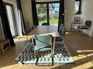 Ein Essbereich mit einem Holztisch, sechs Stühlen, einem gemusterten Teppich und Blick auf einen Garten durch ein Fenster.