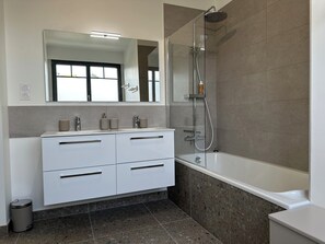 Ein modernes Badezimmer mit einer gläsernen Dusche, einem weißen Waschtisch mit Schubladen und einem großen Spiegel über dem Waschbecken.