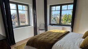 Ein Schlafzimmer mit Bett, Stuhl, Fenster und Blick auf Gebäude.