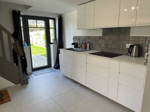A modern kitchen with white cabinets, a black countertop, and a stainless steel kettle. - VILLA ADTHEO (Dinard)
