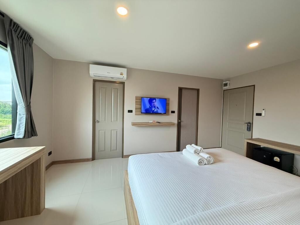 Ein Hotelzimmer mit Bett, Fernseher, Schreibtisch und einem Vorhangfenster.