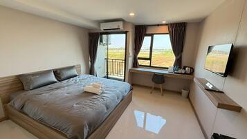 A bedroom with a bed, a desk, a chair, a TV, and a balcony with curtains.