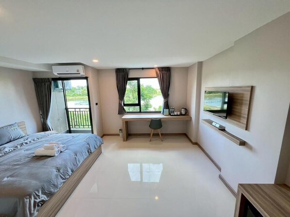 A bedroom with a bed, a desk, a TV, and a window with curtains.