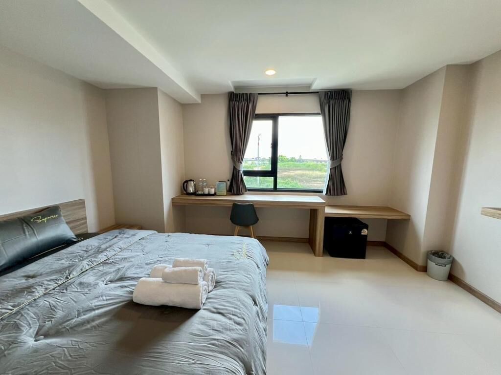 Habitación de hotel con cama, escritorio, silla, ventana con cortinas y vistas al exterior.