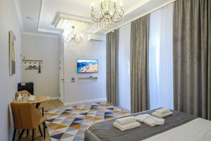 A hotel room with a bed, a TV, a dining table, and a chandelier. - Avant Hotel (Bishkek)