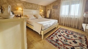 A bedroom with a bed, bedside lamps, a bedside table, a rug, and a window with curtains.