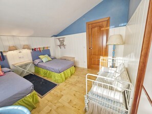 Un dormitorio con dos camas, una mesita, una mesita de noche, una puerta de madera y una lámpara.