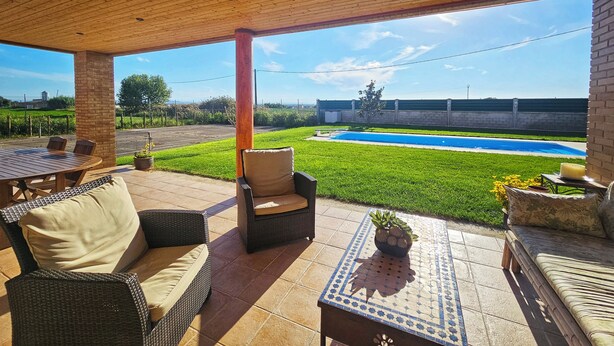 An outdoor patio with wicker furniture, a tiled table, and a view of a swimming pool.