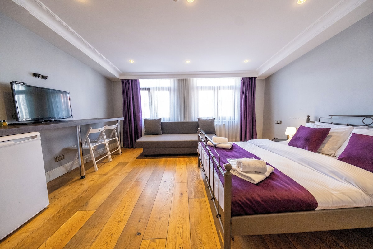 Habitación de hotel con cama, escritorio con televisor, sofá y refrigerador pequeño.