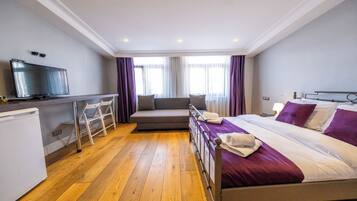Habitación de hotel con cama, escritorio con televisor, sofá y refrigerador pequeño.