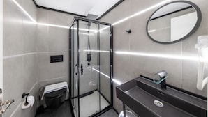 Une salle de bain moderne avec une douche à l’italienne en verre, un lavabo noir doté d’une étagère en verre et un miroir rond fixé au mur.