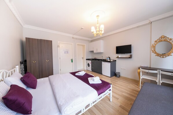 Habitación de hotel con cama, escritorio, televisión, espejo y kitchenette.
