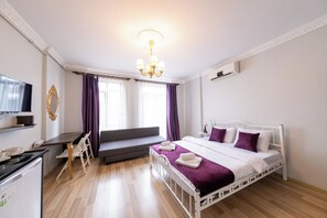 Una habitación de hotel moderna con cama, escritorio, televisión y ventana con cortinas.