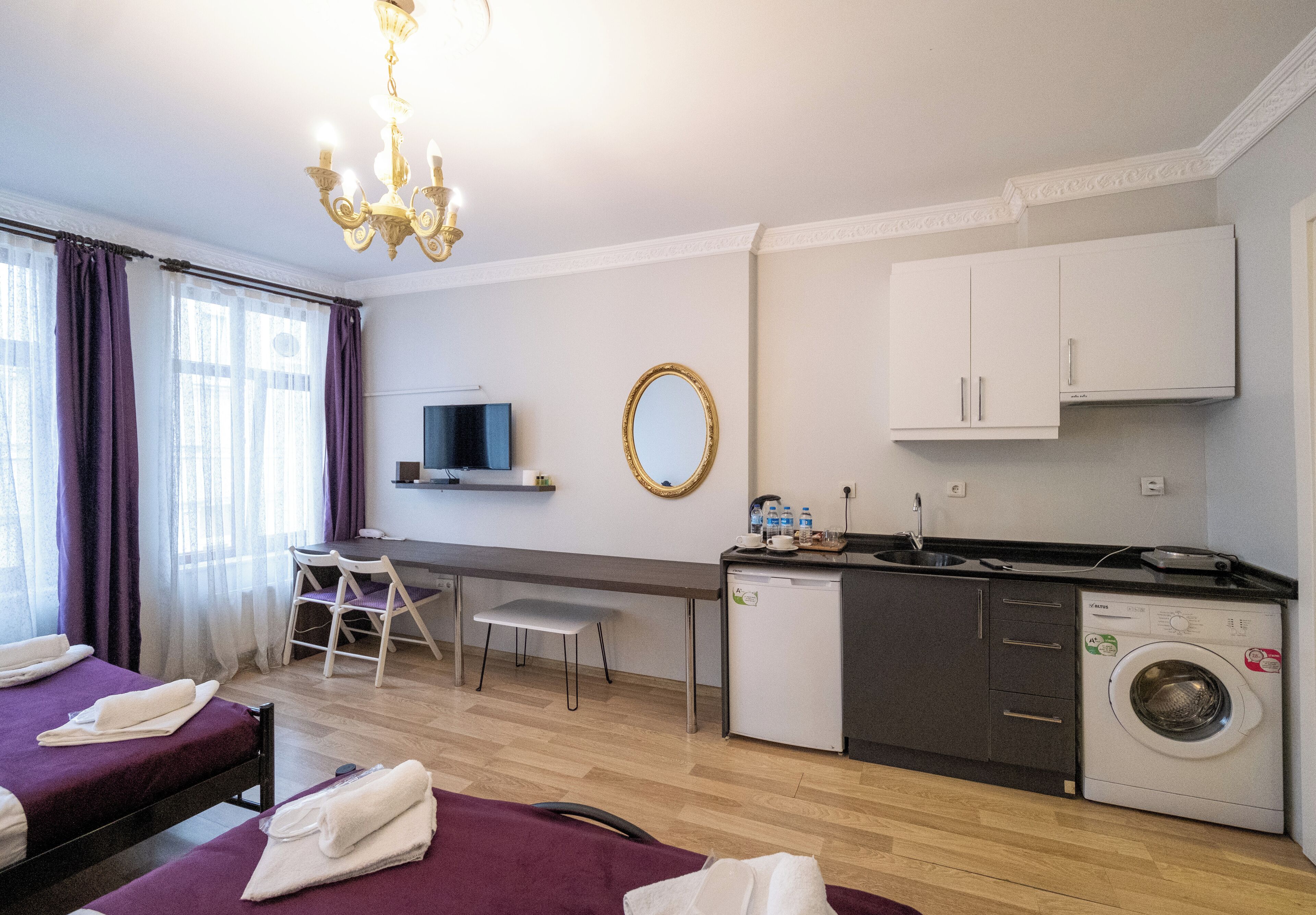 A hotel room with two beds, a desk, a washing machine, and a television.