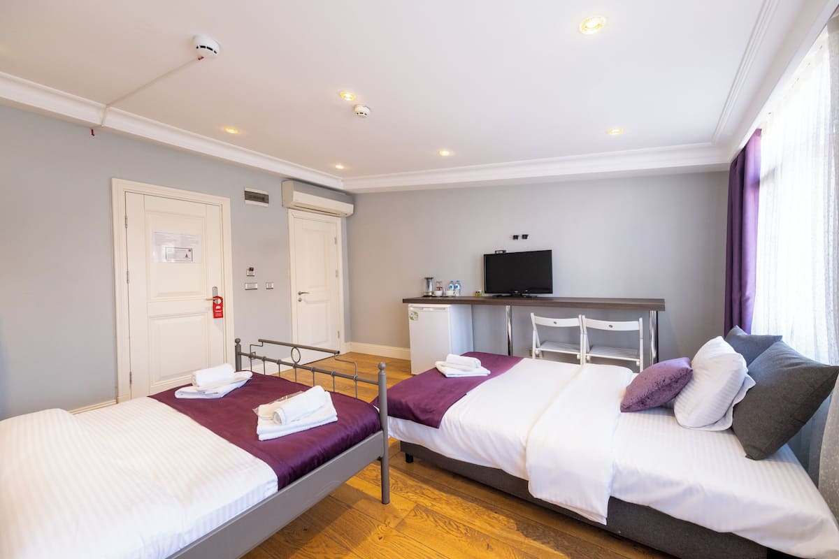 Una habitación de hotel con dos camas, un escritorio, un televisor y una ventana con cortinas.