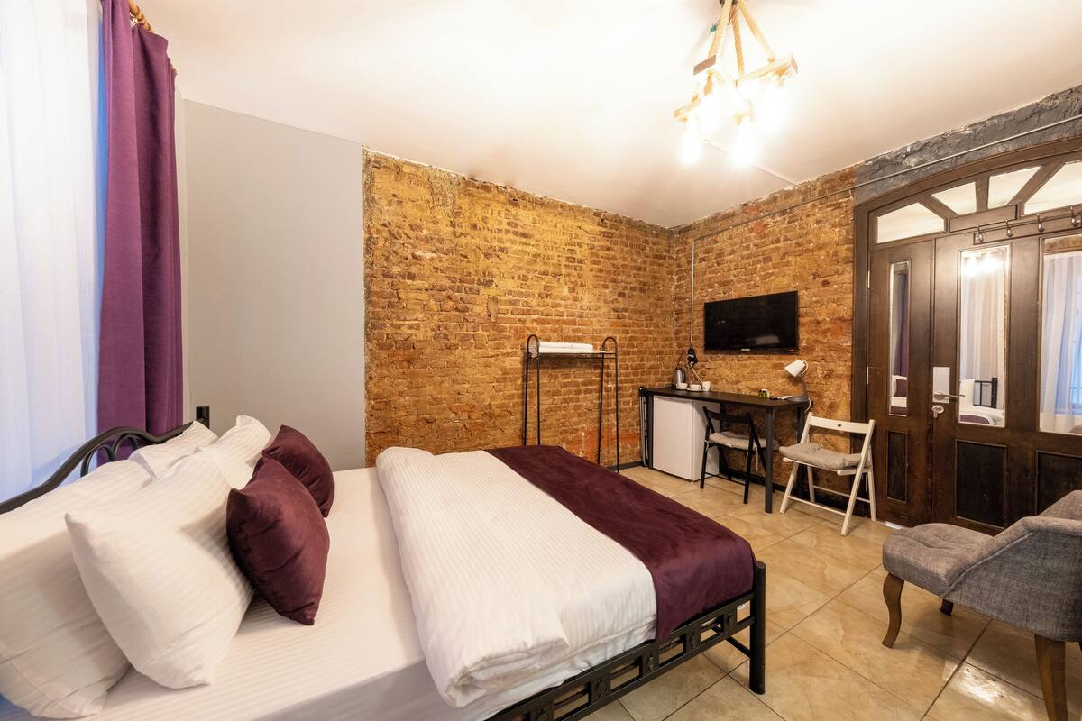 Un dormitorio con cama, escritorio, silla, televisor y pared de ladrillo.