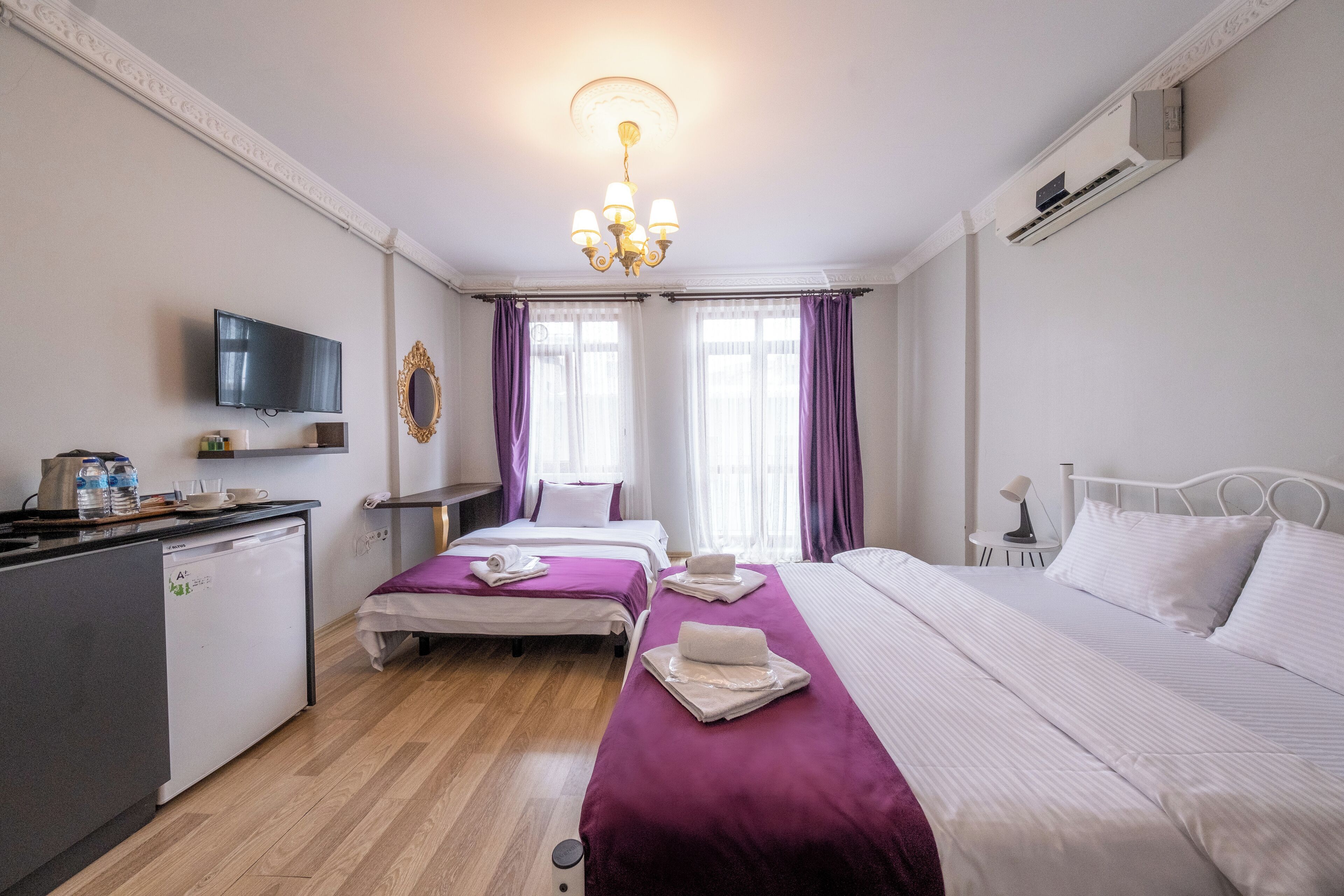 Una habitación de hotel con dos camas, televisión, escritorio con computadora y kitchenette pequeña.