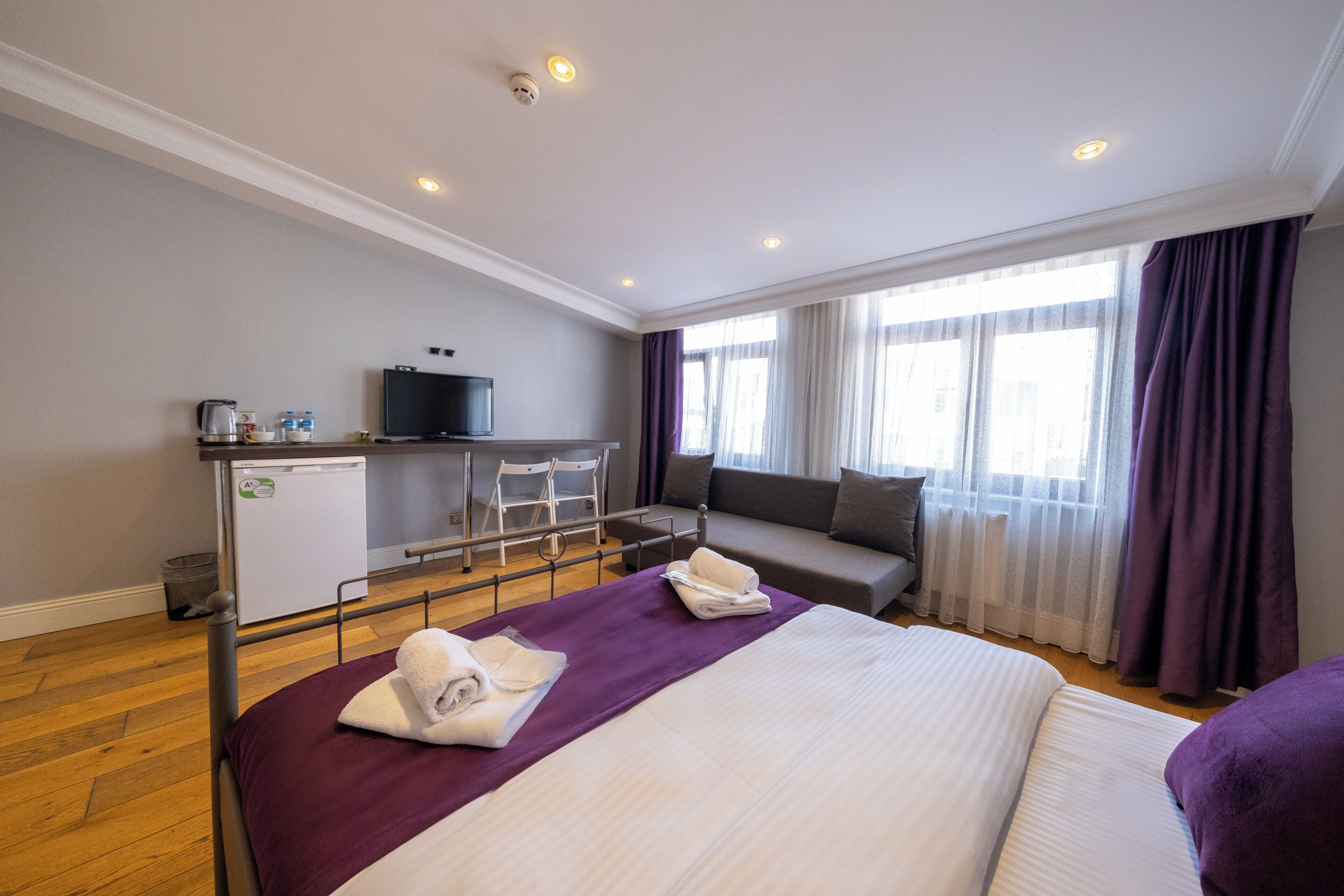 Una habitación de hotel con cama, escritorio con televisor, sofá y ventana con cortinas.