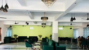 Eine großzügige Lobby mit grünen Sofas, einer Kristallleuchter, Deckenventilatoren und einem Marmorboden.
