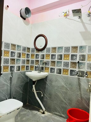 Un bagno con lavandino bianco, specchio, doccia e WC. Le pareti sono rivestite da diverse decorazioni.