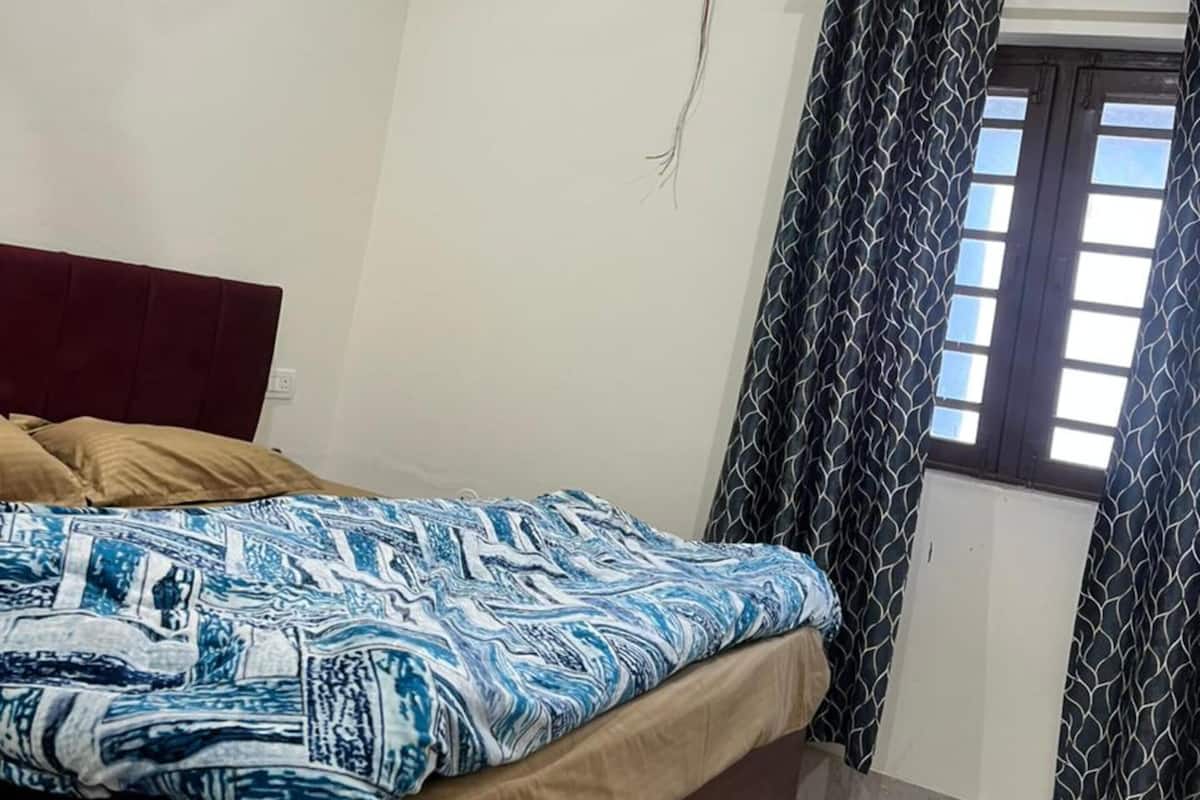 Ein Schlafzimmer mit einem Bett, einem Deckenventilator, einem Fenster mit Vorhängen und einem roten Teppich mit Muster.