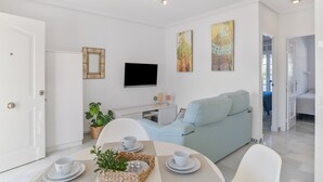 Una sala de estar moderna con un televisor de pantalla plana, un sofá azul claro, una mesa de comedor con tazas y una bandeja, y una puerta blanca.