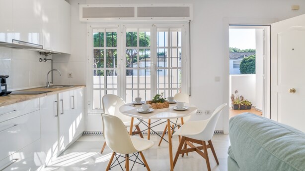 Una cocina moderna con armarios blancos, encimera de madera y un comedor con sillas y mesa blancos.