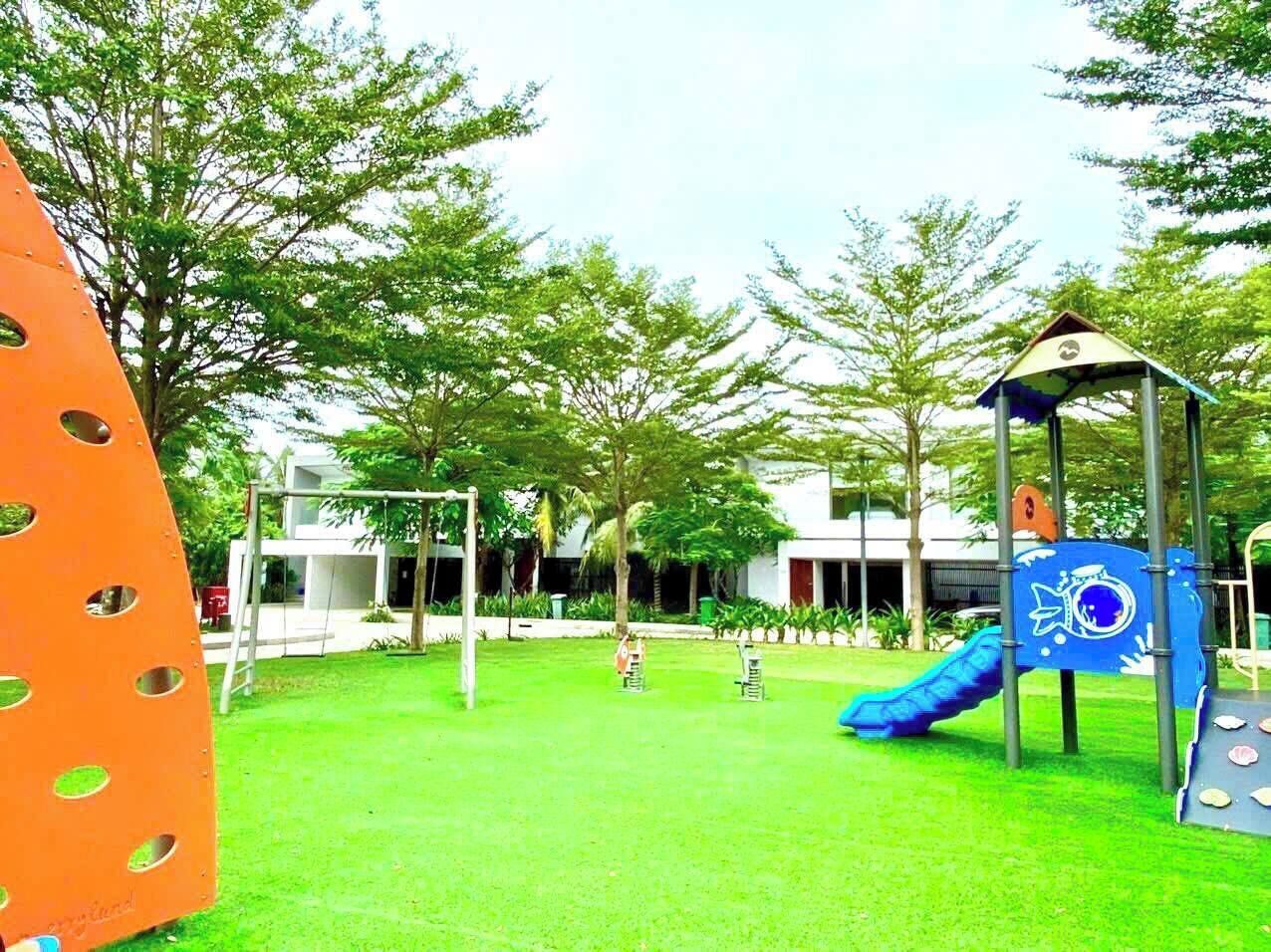 A playground with a slide and swings, surrounded by green grass and trees.