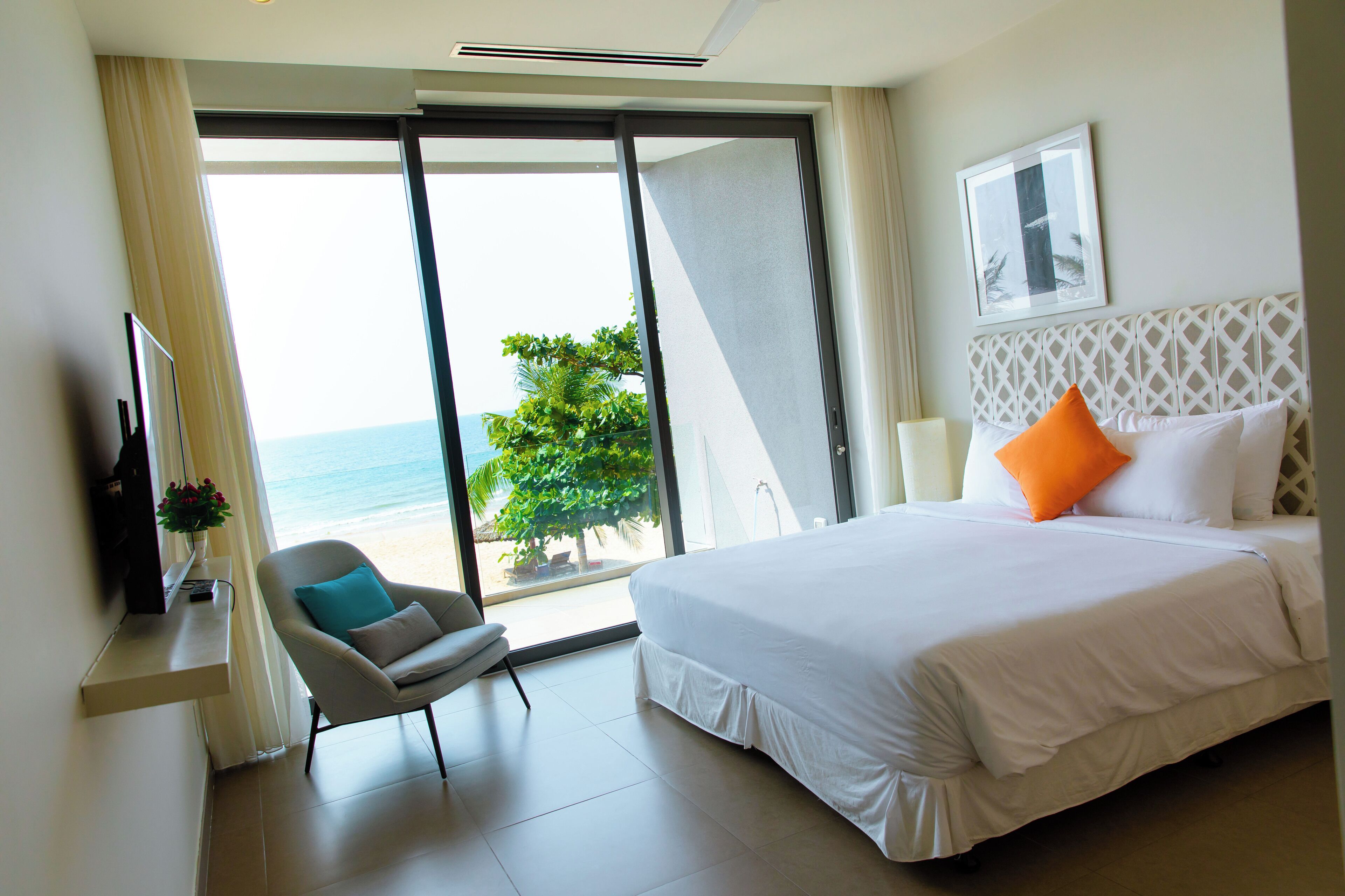 Camera d'albergo con un letto, una sedia, una TV e vista sulla spiaggia.