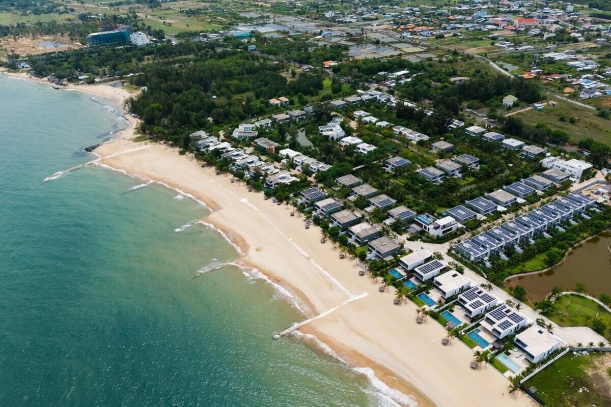Ett flygbildsfoto av ett bostadsområde vid kusten med en strand, hus och solpaneler.
