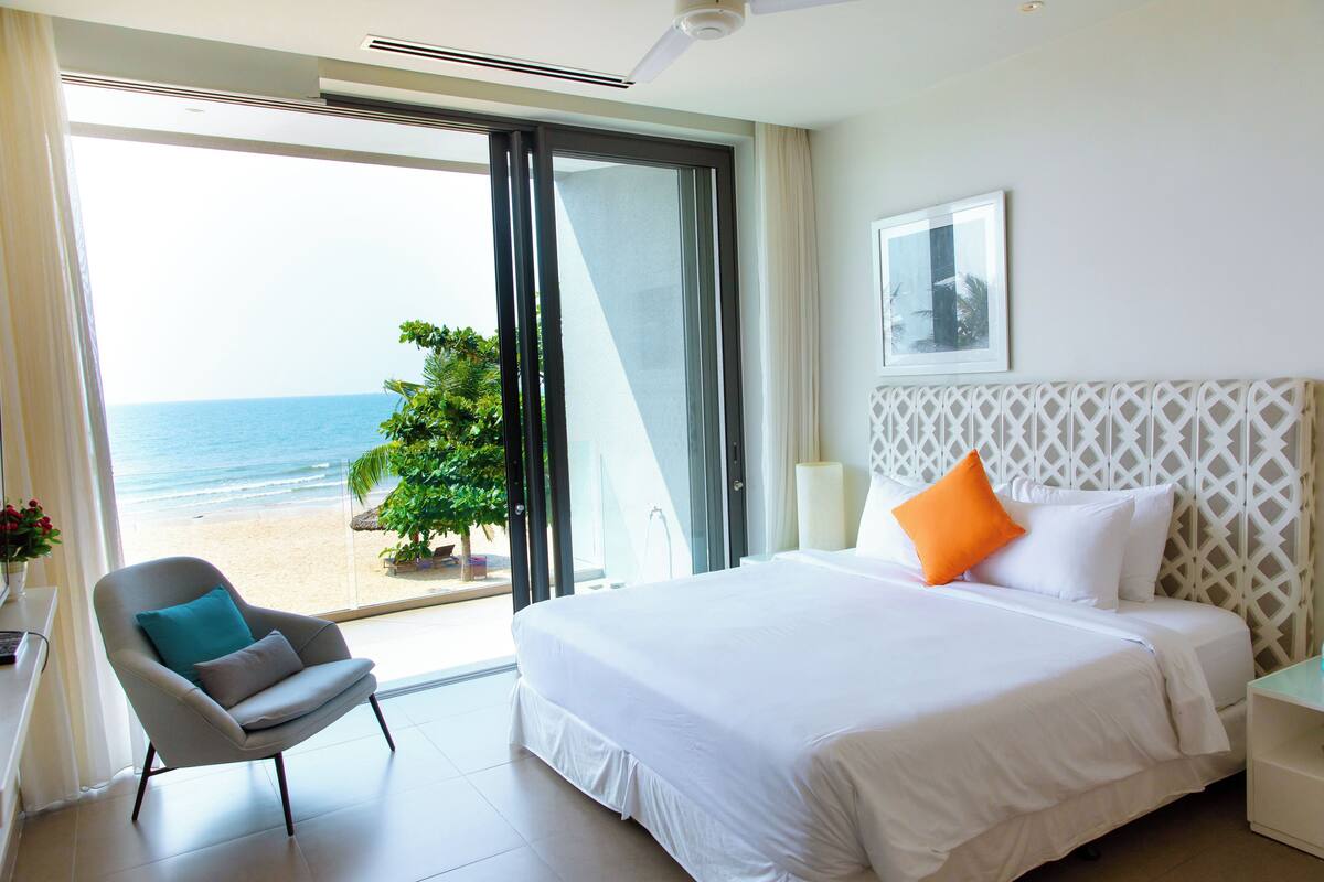 Una habitación de hotel con una cama grande, una silla y vistas a la playa.